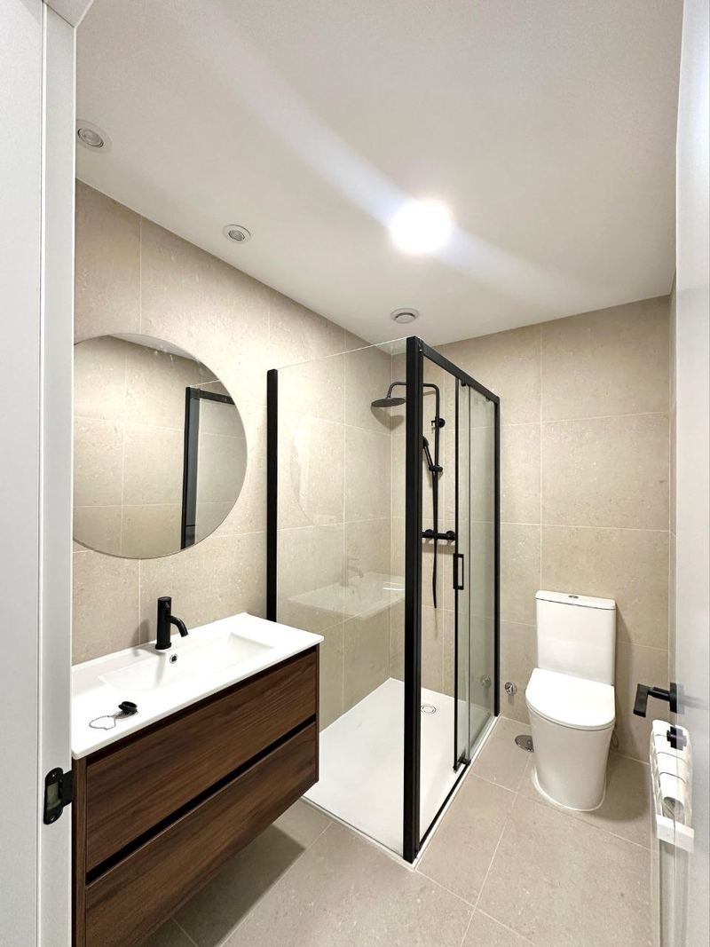 Baño reformado en Vigo con alicatado de gran formato, mueble de madera de dos cajones y grifería negra