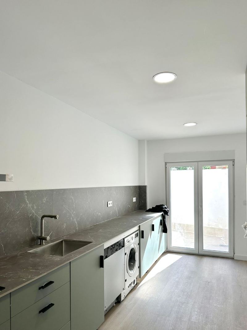 Cocina reformada en Vigo con muebles verdes, encimera y frente de porcelánico gris y salida a la galería