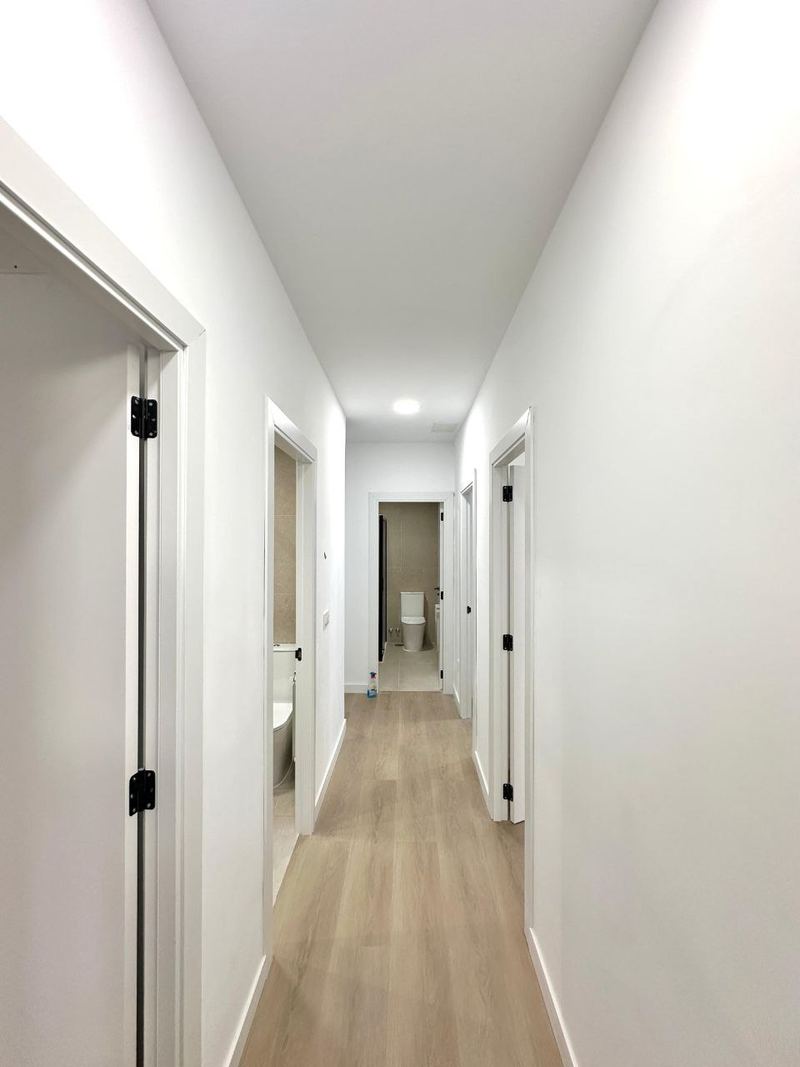 Pasillo de un piso reformado en Vigo con puertas lacadas en blanco, suelo laminado y luces empotradas